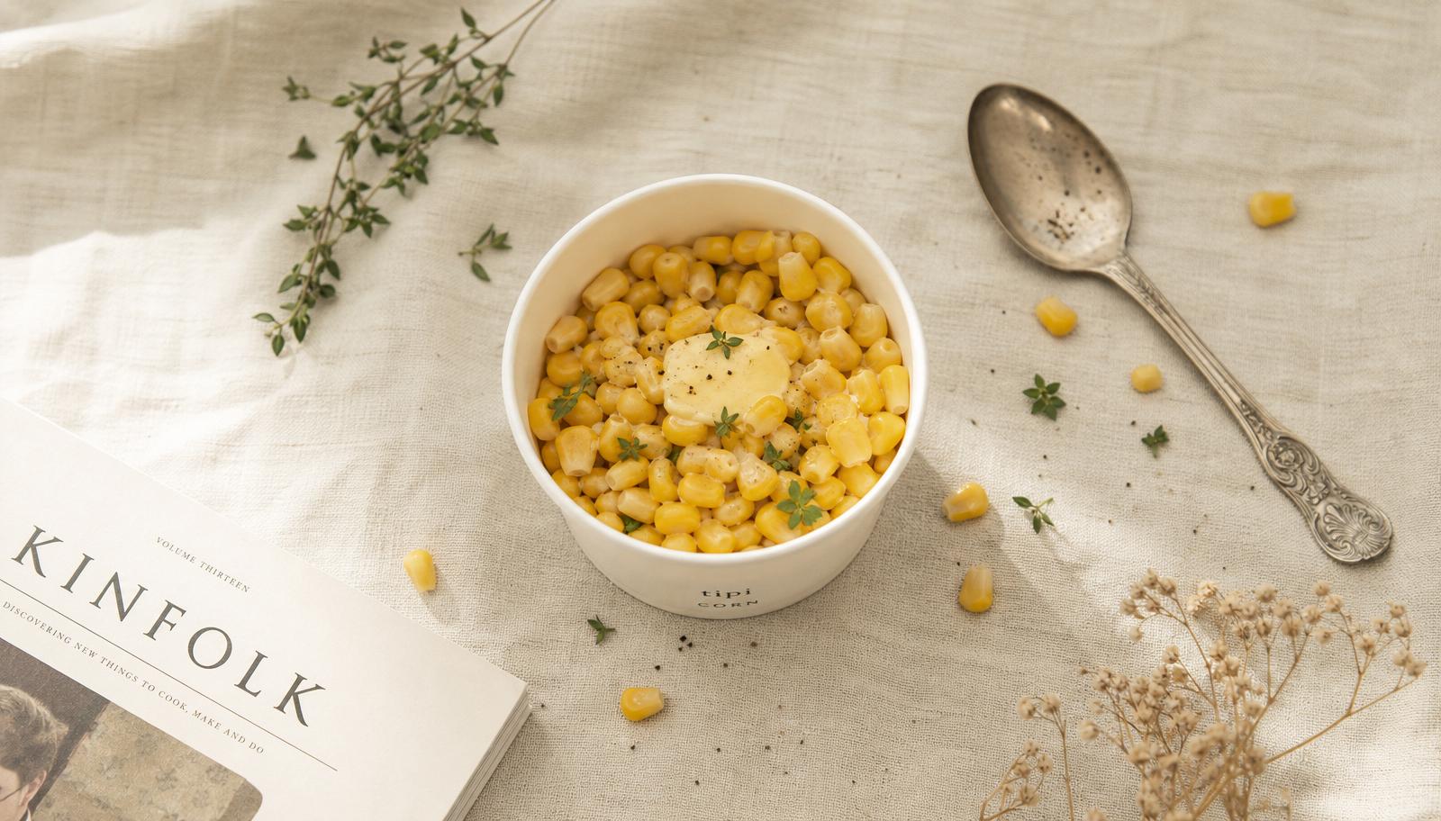 Overhead editorial shot of a paper cup of buttered sweetcorn on cream linen